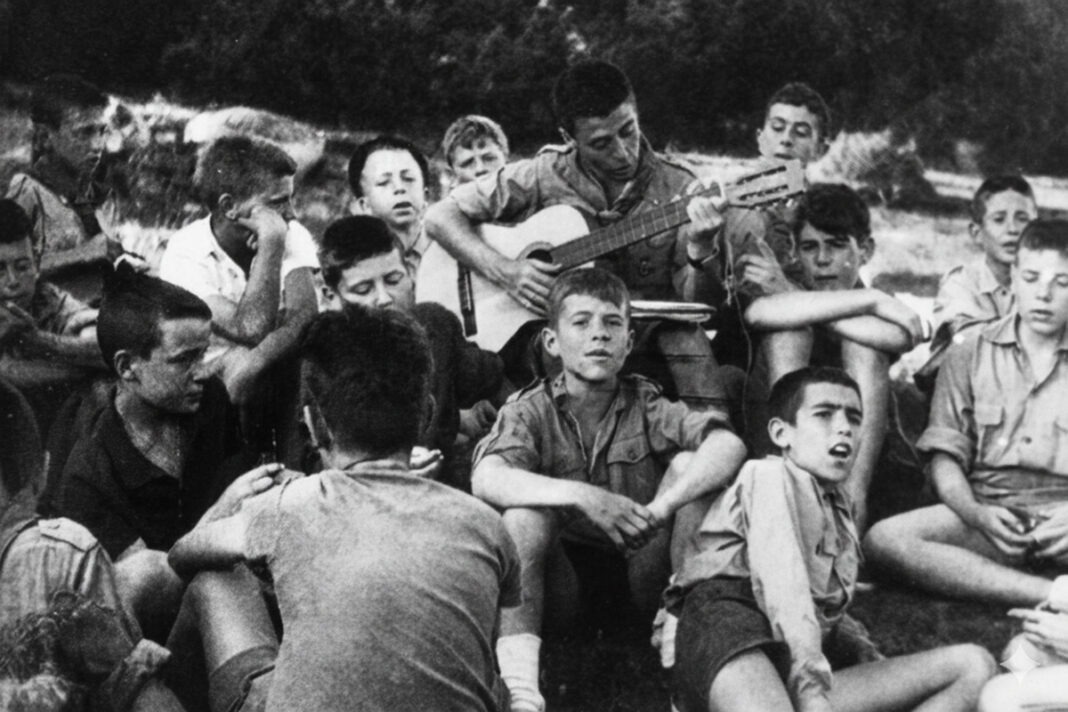 &Agrave;ngel F&agrave;bregues tocant la guitarra vestit d'escolta amb un grup de Minyons Escoltes.